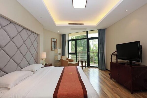 A hotel room with a large bed, a flat-screen TV, a seating area, and a view through the window.