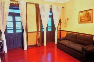 A room with a wooden floor, a black sofa, a door with curtains, and a framed picture on the wall.