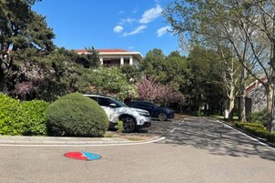A parking area with a red and blue sign, trees, and a building in the background.