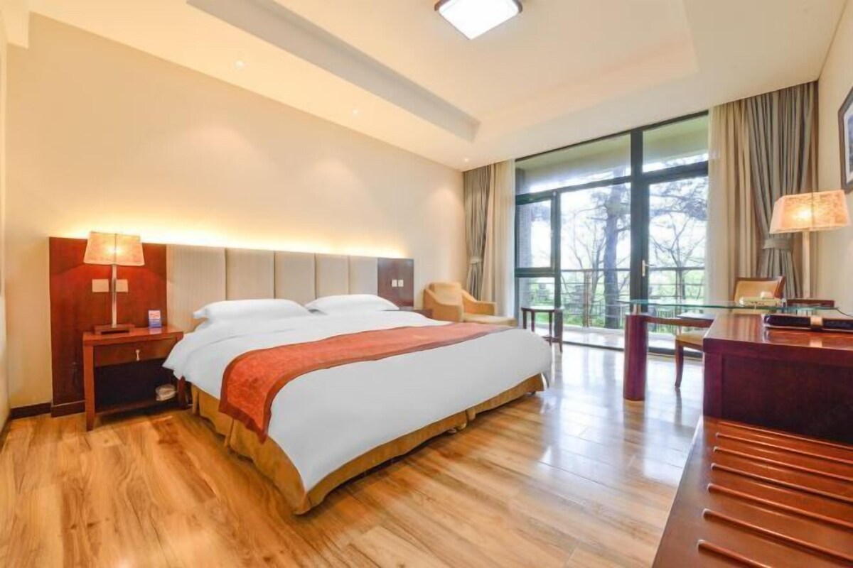 A hotel room with a large bed, a desk, a chair, and a view of the outdoors.
