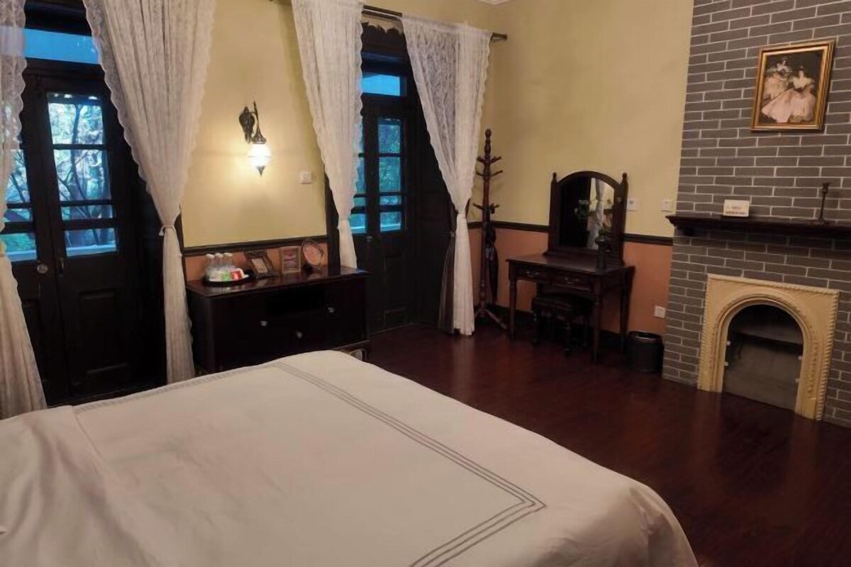 A bedroom with a bed, a dresser, a chair, a fireplace, and curtains.