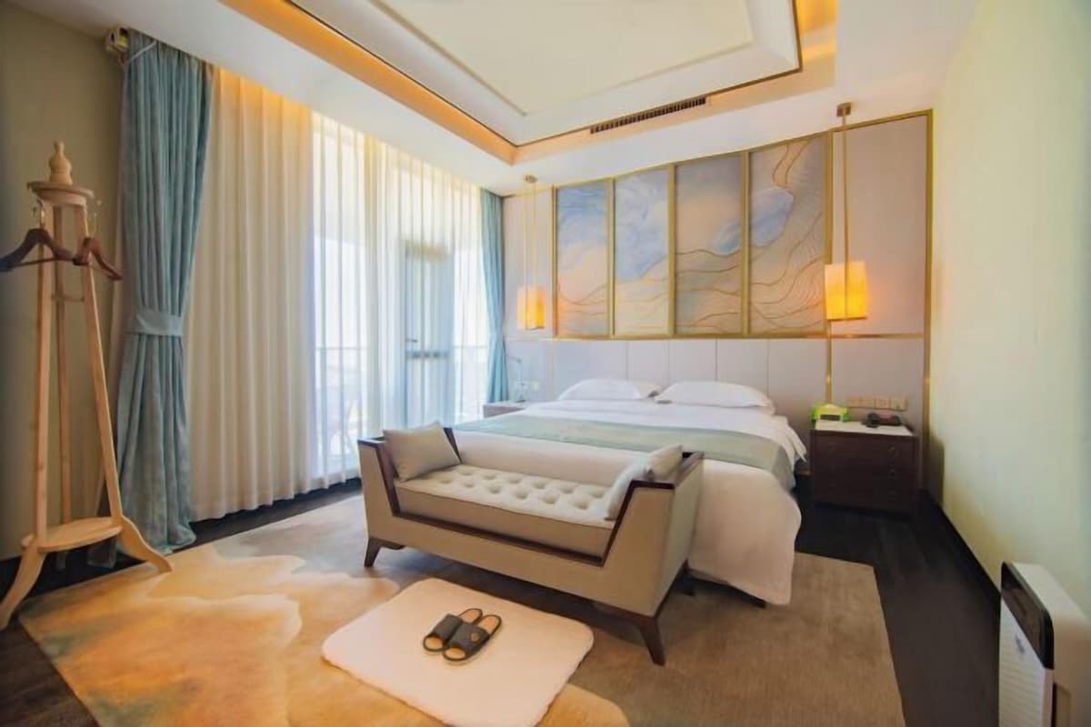 A hotel room with a bed, a sofa, a nightstand, a lamp, and a window with curtains.