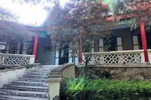Un edificio tradicional con una escalera de piedra que conduce a una entrada con portones, rodeado de follaje.