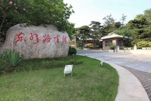 Une grande pierre ornée de caractères chinois, une entrée dallée et un bâtiment en arrière-plan.