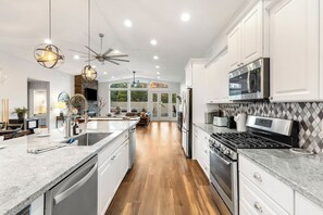 Una cocina amplia con una isla central, electrodomésticos de acero inoxidable y un ventilador de techo moderno.