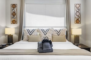 Una habitación de hotel con una cama grande, dos lámparas de noche, un adorno de pared y una ventana con cortinas.