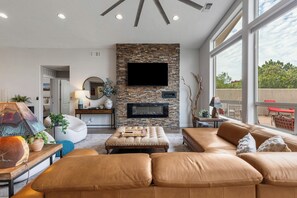 Ein modernes Wohnzimmer mit Kamin aus Stein, Ledersofas und einem großen Fenster mit Blick ins Freie.