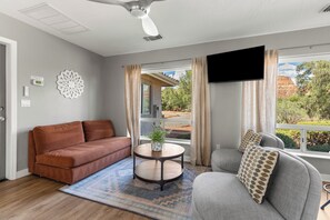 Ein modernes Wohnzimmer mit einem braunen Sofa, einem grauen Sessel, einem runden Couchtisch und einem flachbildfernseher an der Wand.