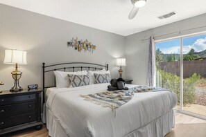 A bedroom with a bed, bedside lamps, a wall art piece, and a view of the outdoors through a sliding glass door.