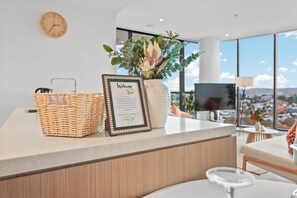 A reception desk with a welcome sign, a wicker basket, a vase with flowers, and a city view through large windows.