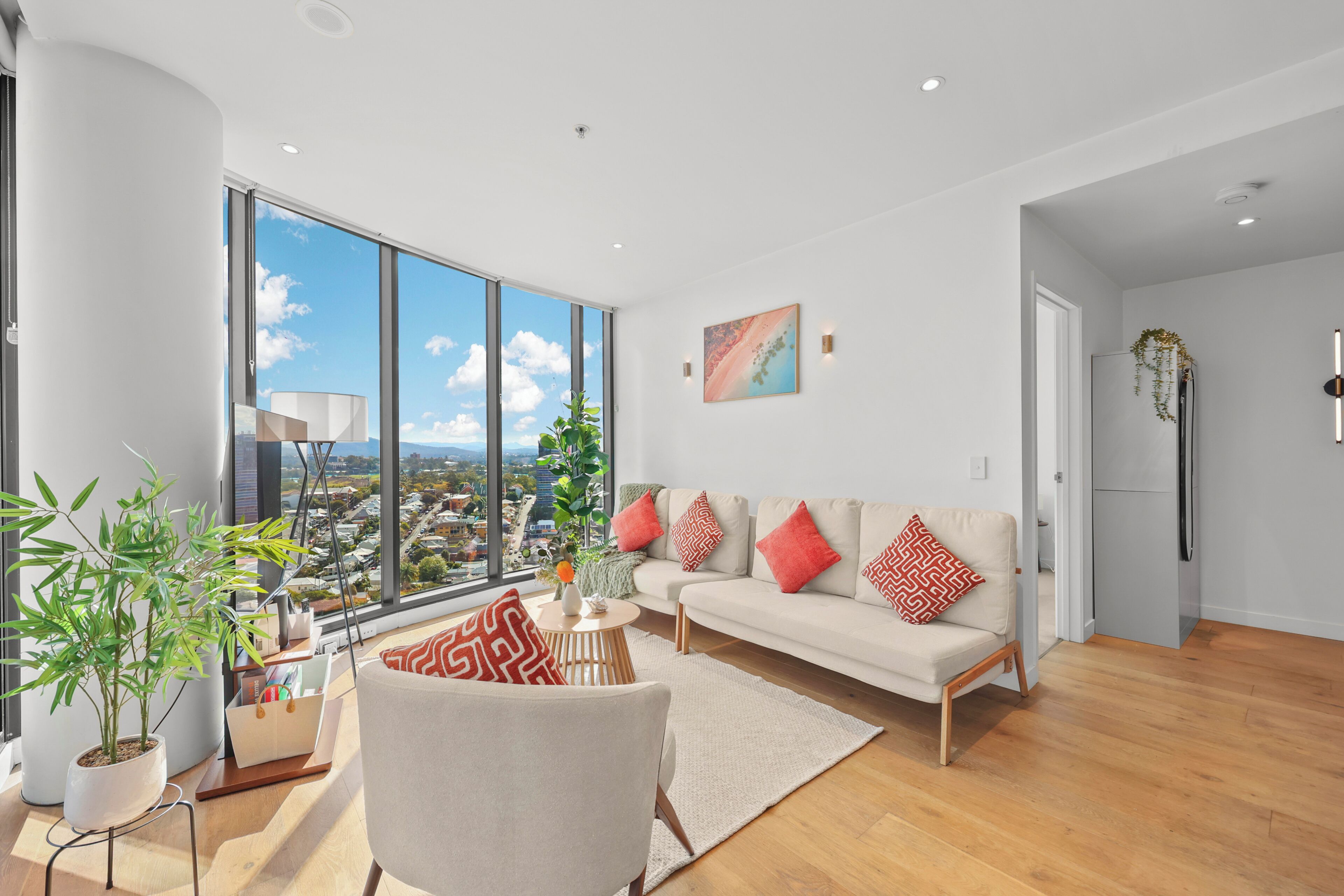 A modern living room with a large window, a sofa, a chair, and a potted plant.