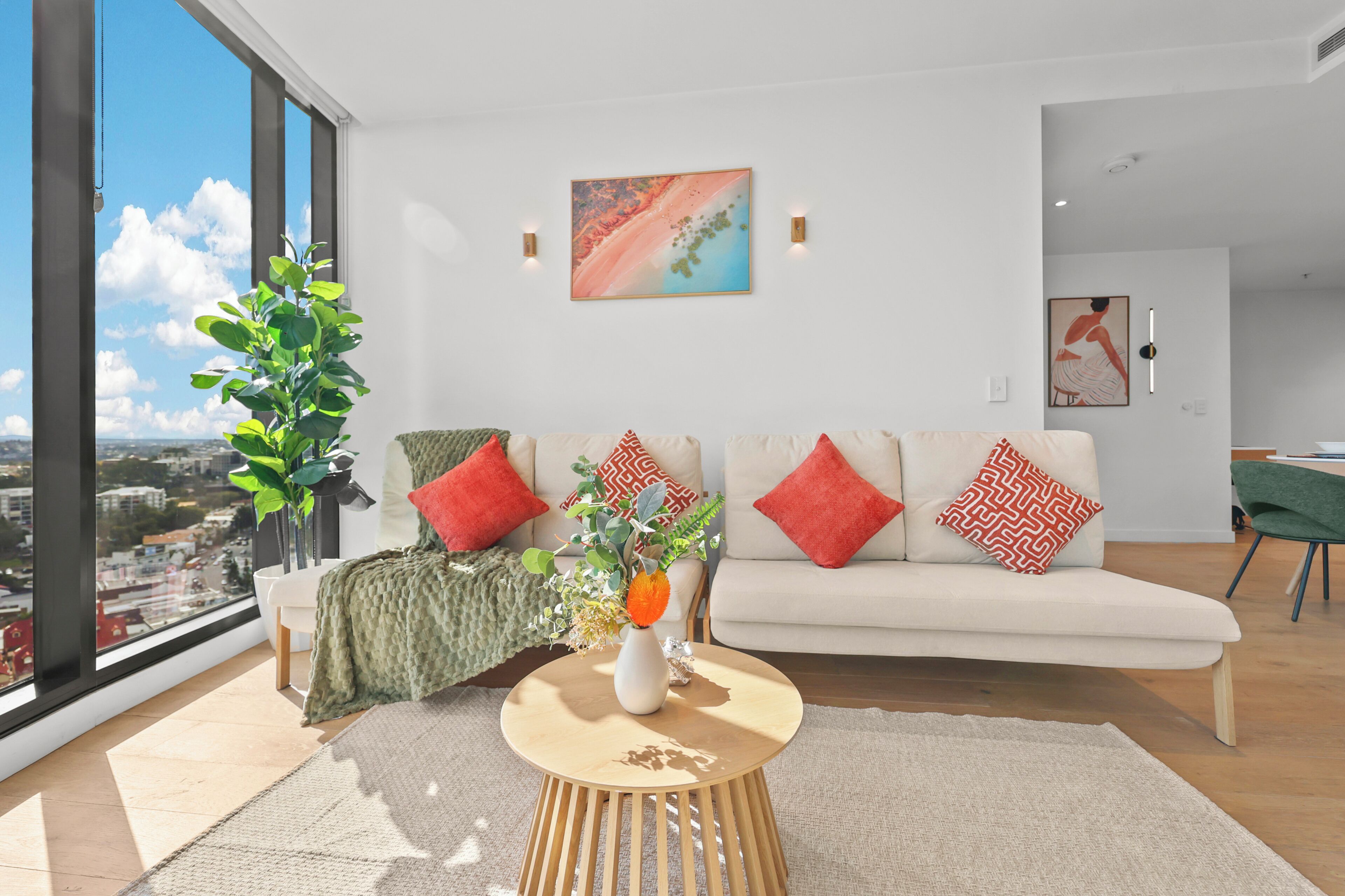 A modern living room with a large window, a sofa, a coffee table, and a potted plant.