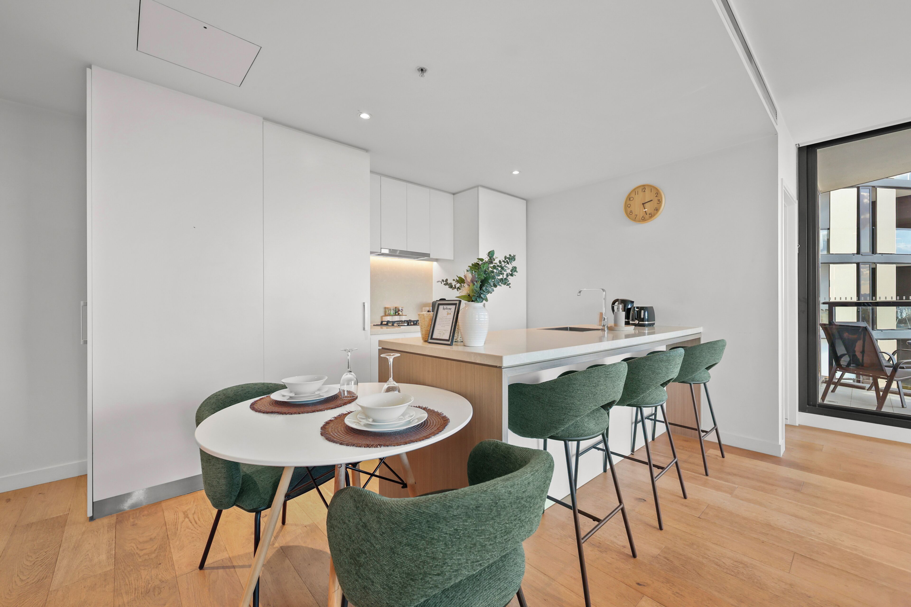 Una cocina moderna con una isla central, taburetes de bar y una mesa de comedor con sillas verdes.