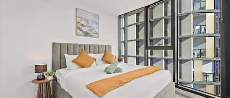 A modern bedroom with a large bed, a nightstand, a lamp, and a painting on the wall.
