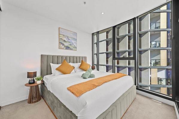 A modern bedroom with a large bed, a nightstand, a lamp, and a painting on the wall.