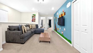 Un salon avec un canapé d’angle, une table basse en bois et un mur décoré sur le thème de Mario.