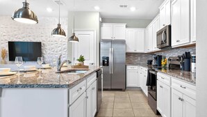 Eine moderne Küche mit weißen Schränken, einem Edelstahl-Kühlschrank, Granit-Arbeitsplatten und Pendelleuchten.