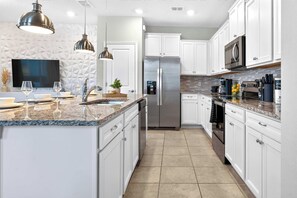 A modern kitchen with white cabinetry, a stainless steel refrigerator, granite countertops, and pendant lighting. - 5BR Private Pool | Windsor Island Resort (Davenport)