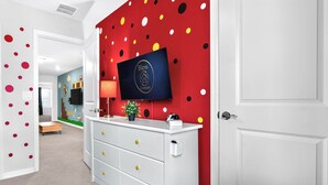 Ein Flur mit roter Wand, einem Logo, einer weißen Kommode mit Schubladen und einem darüber montierten Fernseher.