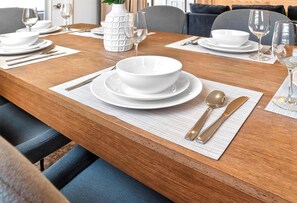 Une table à manger dressée avec de l’assiette, des bols et des couverts blancs, le tout posé sur un set de table texturé.