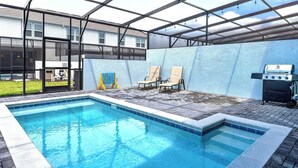 Ein Schwimmbad mit Glasumrandung, Grill und Liegestühlen.