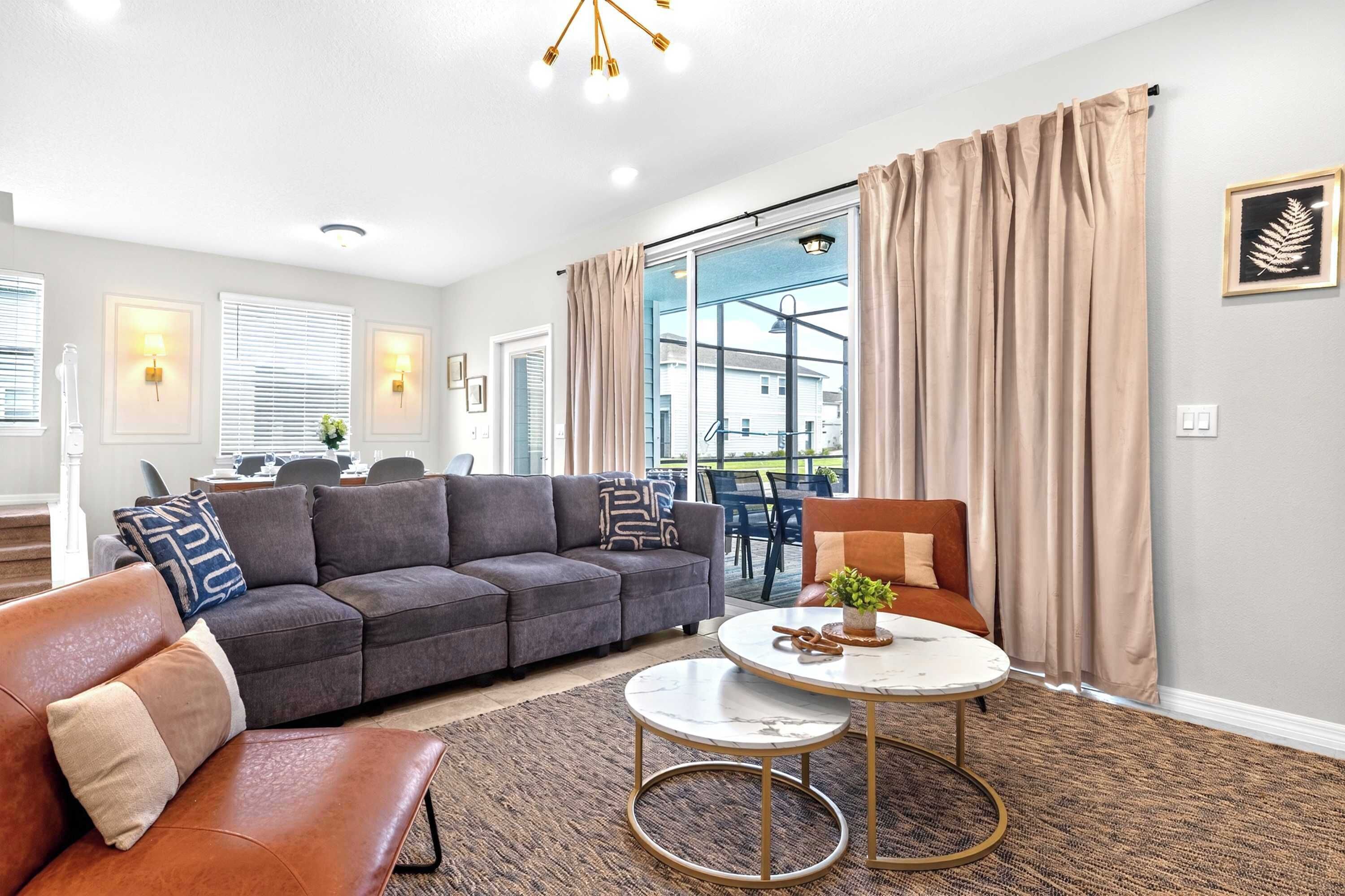 Ein modernes Wohnzimmer mit einem grauen Ecksofa, einem runden Couchtisch und einem braunen Ledersitzhocker.