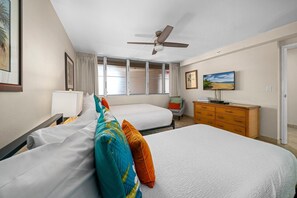 Ein Hotelzimmer mit zwei Betten, einem Deckenventilator, einem Schminktisch und einem Fenster mit Vorhängen.