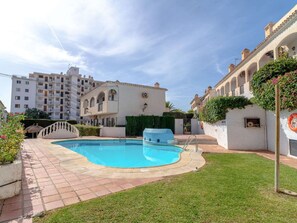 Una piscina con zona pavimentada alrededor, junto a un edificio de fachada blanca y ventanas arqueadas.