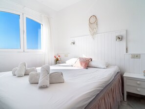 Una camera d'albergo con un letto grande, biancheria da letto bianca, un comodino, una lampada a parete e una finestra con tende.