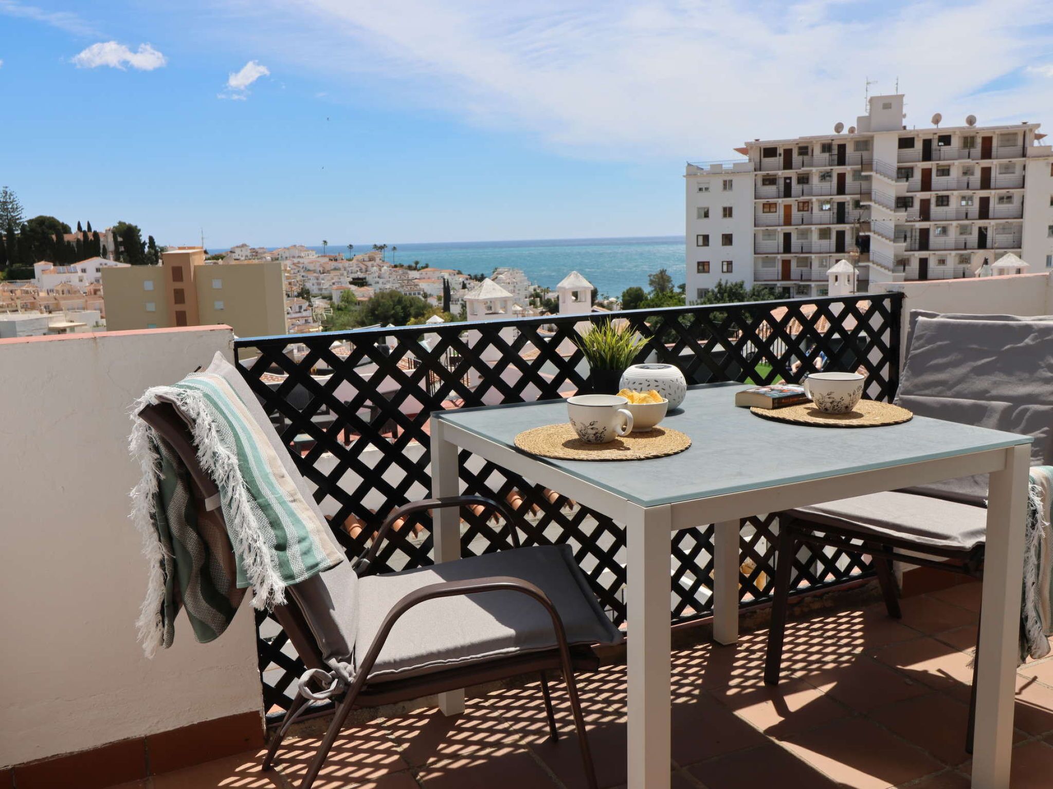Ein Balkon mit Tisch, Stühlen und Blick auf das Meer und die Gebäude.