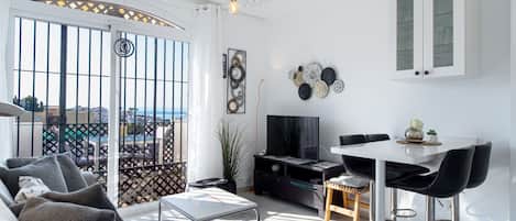 Ein modernes Wohnzimmer mit Sofa, Fernseher, Essbereich und einem Balkon mit Blick.