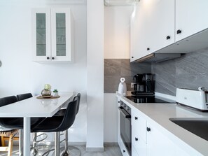 Una cocina moderna con alacenas blancas, salpicadero de mármol y un comedor con mesa blanca y sillas negras.
