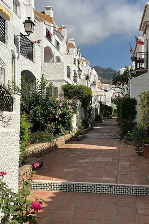 A narrow street with white buildings, a tiled pathway, and greenery. - Apartment  by Interhome (Nerja)
