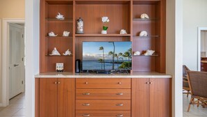 A wooden entertainment center with a flat-screen TV, decorative shells, and a small potted plant. - Kapalua Bay Villa 22B4 Gold Oceanfront 1 Bedroom (Lahaina)