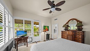 A bedroom with a bed, a ceiling fan, a dresser, a television, and a door leading to a balcony with a view of palm trees. - Kapalua Bay Villa 22B4 Gold Oceanfront 1 Bedroom (Lahaina)