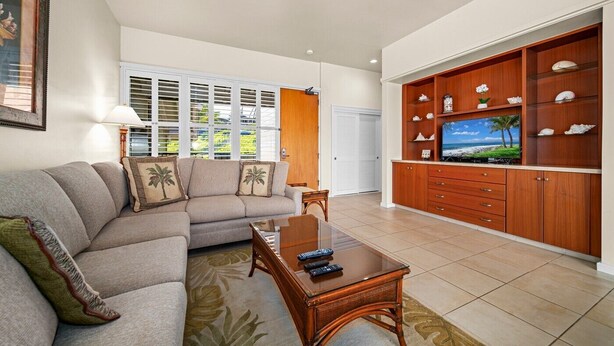A living room with a sectional sofa, a coffee table, a TV on a wooden cabinet, and a window with blinds. - Kapalua Bay Villa 22B4 Gold Oceanfront 1 Bedroom (Lahaina)