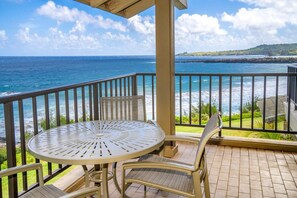 A balcony with a table and chairs, overlooking a coastal view with the ocean and a distant landmass. - Kapalua Bay Villa 22B4 Gold Oceanfront 1 Bedroom (Lahaina)