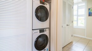 A laundry room with two stacked front-loading washing machines and a door leading to another room. - Kapalua Bay Villa 22B4 Gold Oceanfront 1 Bedroom (Lahaina)