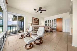 A spacious living area with a balcony, a ceiling fan, and a large window overlooking a beach. - Kapalua Bay Villa 22B4 Gold Oceanfront 1 Bedroom (Lahaina)