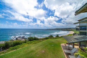 Ein Küsteneigentum mit Meerblick, einer Rasenfläche und einem Gebäude mit einem Balkon, der auf den Strand blickt.