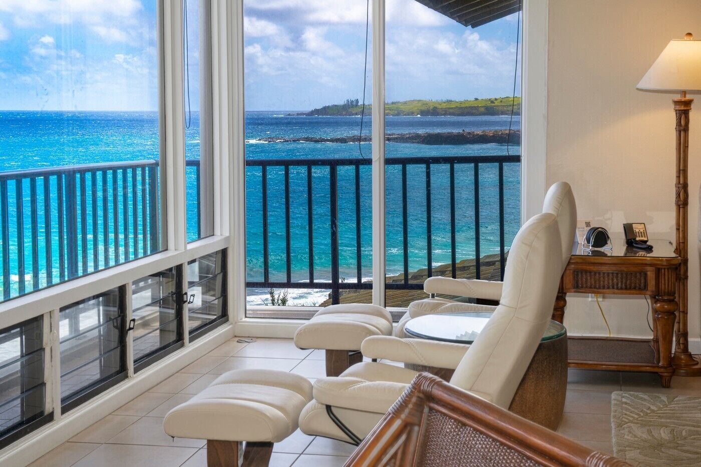 A balcony with a view of the ocean, a white chair, a small table with a lamp, and a telephone.