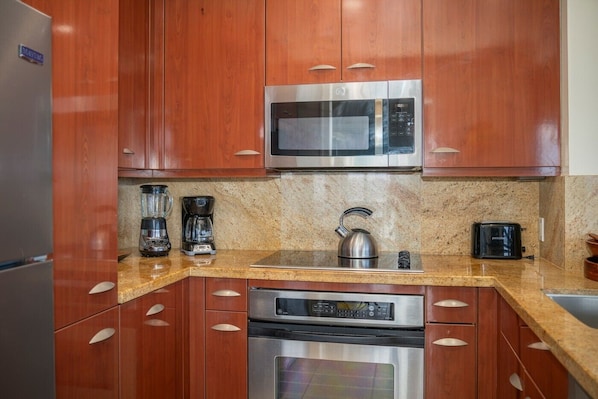 A kitchen with wooden cabinets, a stainless steel microwave, a kettle, a coffee maker, and a toaster. - Kapalua Bay Villa 22B4 Gold Oceanfront 1 Bedroom (Lahaina)