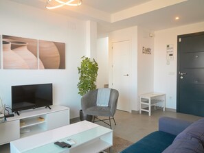 Uma sala de estar moderna com televisão de tela plana, uma poltrona cinza, uma mesinha e um sofá.