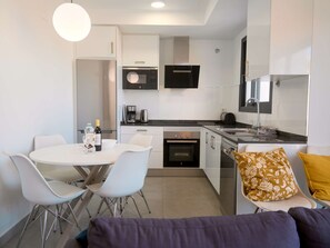 Uma cozinha compacta equipada com micro-ondas, cafeteira e forno. Há uma área de refeições com mesa e cadeiras.