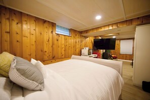 A bedroom with wooden panel walls, a bed with white bedding, a television mounted on the wall, and a small table with a microwave. - The Westside Hideaway with Hot Tub and Patio (Minneapolis)