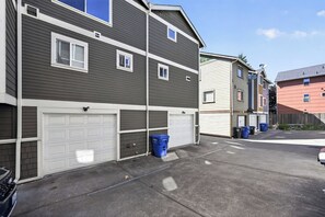 A residential building with two garages, a satellite dish, and a row of blue recycling bins. - Stylish Townhome Near Alki Beach & Downtown (Seattle)