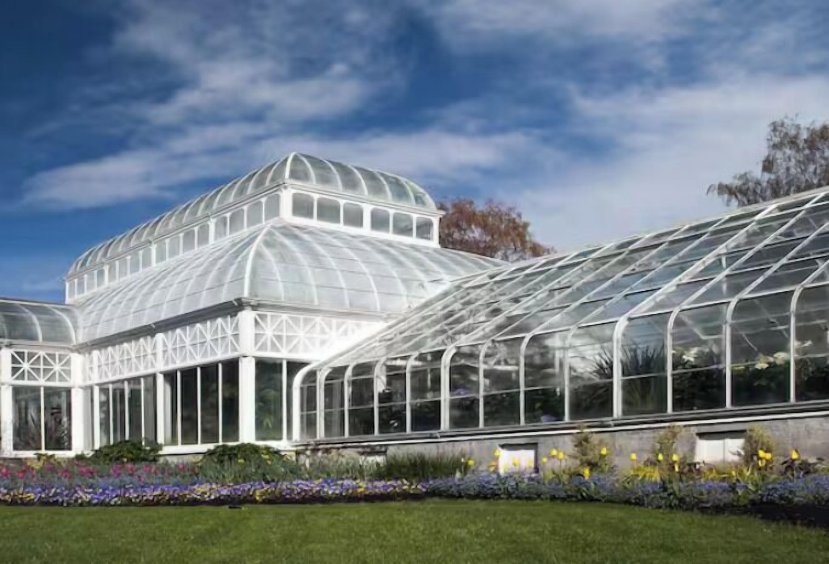 A large greenhouse with a glass roof and walls, surrounded by a well-maintained garden.