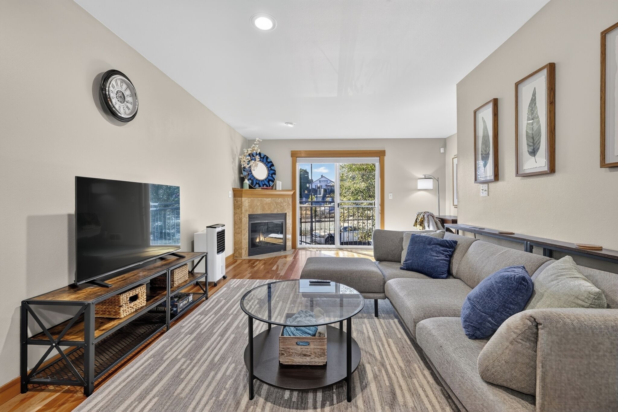 A modern living room with a flat-screen TV, a glass coffee table, a sofa, and a fireplace.