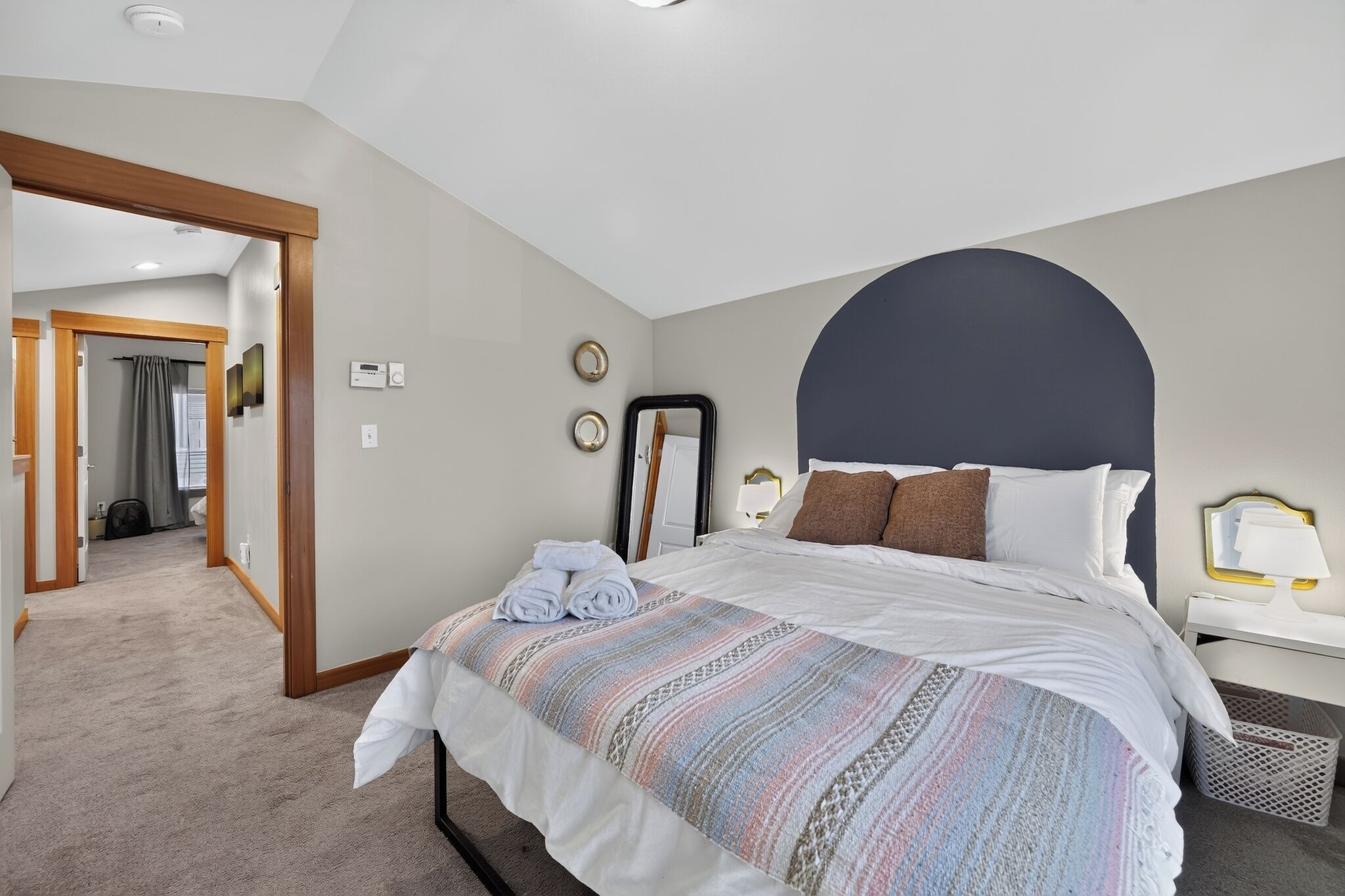 A hotel room with a large bed, a bedside table, a mirror, and a door leading to a bathroom.