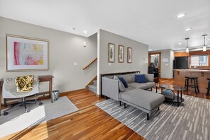 A modern living room with a sofa, a desk, and a staircase leading to an upper level. - Stylish Townhome Near Alki Beach & Downtown (Seattle)